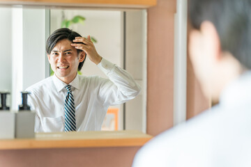 洗面所で頭皮の生え際を機にする若いアジア人男性（薄毛・脱毛・AGA・抜け毛）
