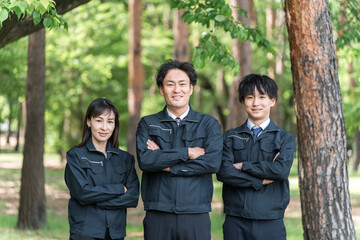 森林の中で腕組みをする林業・土木業の作業着姿の男女の作業員
