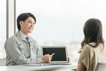 Obraz premium スマホを使いマイホーム・リフォームの見積もり・シュミレーションを提示する作業着姿の男性と女性客 