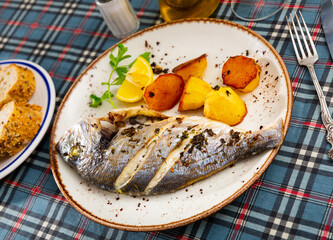 Baked in oven dorado fish with lemon and potatoes served on plate