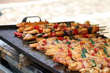 Close-up of skewered chicken pieces, bell peppers, and other vegetables grilling on a hot flat iron plate, showcasing vibrant colors and a delicious smoky aroma