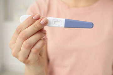 Woman holding pregnancy test indoors, closeup view