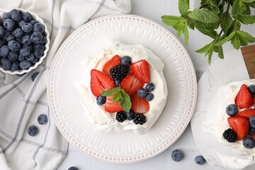 Pavlova cake (meringue dessert) with whipped cream, fresh berries and mint on white table, flat lay