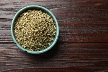 Dried oregano in bowl on wooden table, top view. Space for text