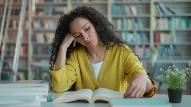 Tired Latino arabian woman sitting reading book studying knowledge exam preparation lesson lecture session student girl female library boredom intelligence education desk college learning university