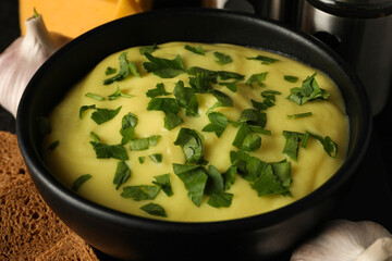 Cheese soup in a black bowl with greens close-up