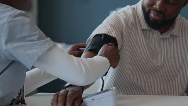 Close up view of female physician applying cuff of blood pressure monitor to arm of Black man during appointment at doctors office