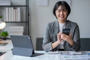 Asian businesswoman smiling using smartphone in modern office