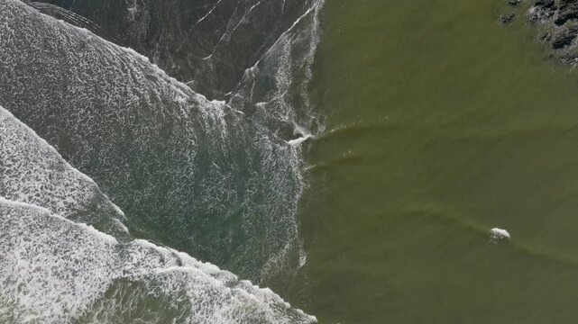 Aerial: Abstract textures of waves crashing on the ocean shoreline in Marokopa, Waikato, New Zealand.
