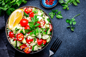 Vegetarian Tabbouleh Middle Eastern salad with bulgur, tomatoes, cucumbers and parsley.. Black background, top view