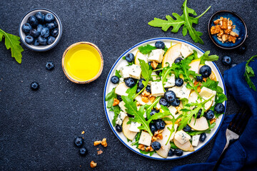 Tasty salad with pears, blueberries, roquefort cheese, arugula and nuts. Black background, top view