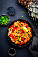 Stir fryed chicken slices with pineapple, paprika, chives, garlic, ginger, soy sauce and sesame seeds. Black background, top view
