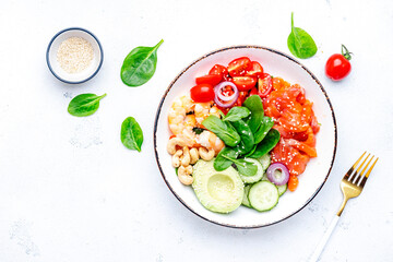 Seafood salad poke bowl with shrimp, salmon, avocado, spinach, cucumber, tomato, cashew, sesame seeds. White background, top view