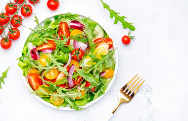 Vegan vegetable salad with tomatoes, cucumber, onion, lettuce and arugula. White background, top view