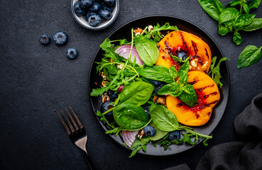 Vegan delicious salad with grilled peaches, fresh blueberries, red onion, walnuts, basil and mixed herbs, black background, top view