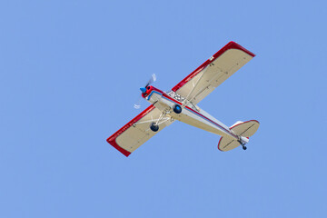 Overhead tail wheel airplane. Isolated on clear blue sky, high wing aircraft in flight at altitude. Red white and blue paint on piston powered propeller driven aircraft