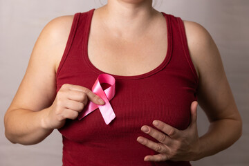 A woman is wearing a vibrant red tank top, and she is proudly holding a pink ribbon against her chest as a meaningful gesture