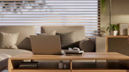 A laptop, books, and headphones on a minimal wooden coffee table in a cozy contemporary living room.