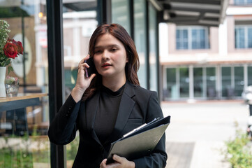 Fototapeta premium A professional businesswoman in a black suit is talking on the phone while walking outdoors.