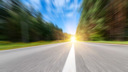 Blurred road and blue blurred sky and forest with a shining sun.