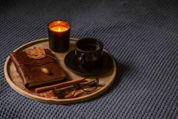 Cozy autumn setup with coffee cup, lit candle and journal on wooden tray.