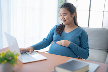 Pregnant asian woman using laptop at home pregnant businesswoman typing on laptop working on remote project in home office pregnancy concept