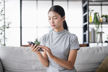 Asian Woman controlling smart home. mobile phone with smart home app in living room. touch screen ai technology. Remote home control system