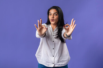 A young woman of Indian descent, wearing a white striped shirt and black smartwatch, stands against...