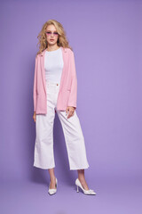 Fashion female model in pink jacket, white culottes jeans, shoes, top and sunglasses.