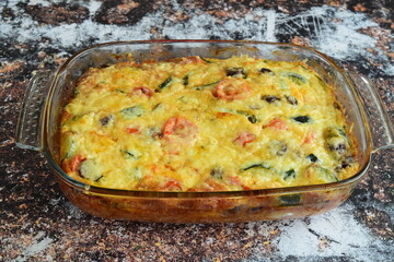 Vegetarian casserole with zucchini cheese and cherry tomatoes close-up in a baking dish. 
