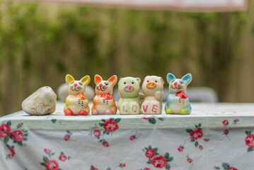 Four colorful ceramic animal figurines, including rabbits and a pig, are arranged on a floral tablecloth with the word 