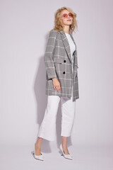 Fashion female model in grey checked coat, white culottes jeans, top, heels shoes, and sunglasses.