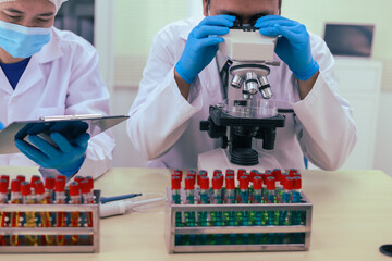 Two male researchers are conducting chemical research in a science lab, carefully analyzing substances at a desk filled with scientific instruments and chemical solutions in a well-organized