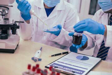 Two male researchers are conducting chemical research in a science lab, carefully analyzing substances at a desk filled with scientific instruments and chemical solutions in a well-organized