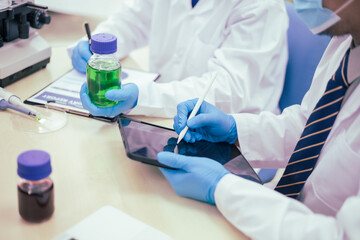 Two male researchers are conducting chemical research in a science lab, carefully analyzing substances at a desk filled with scientific instruments and chemical solutions in a well-organized