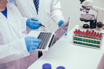 Two male researchers are conducting chemical research in a science lab, carefully analyzing substances at a desk filled with scientific instruments and chemical solutions in a well-organized