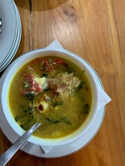 Red Snapper fish spicy soup Sour curry in a white bowl with garlic, tomatoes, vegetable and chili turmeric sauce and various spices, over wooden table. delicious food.
