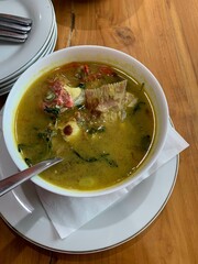 Red Snapper fish spicy soup Sour curry in a white bowl with garlic, tomatoes, vegetable and chili turmeric sauce and various spices, over wooden table. delicious food.