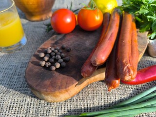 juicy fried sausages lying on the table surrounded by vegetables and herbs.