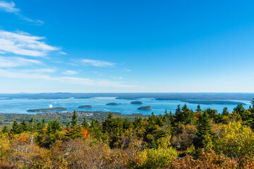 Viewpoint perspective of fall foliage and trees in autumn from a hiking area past the tree line viewing a cruise ship sailing through distant islands in blue water on a blue sky day with some clouds