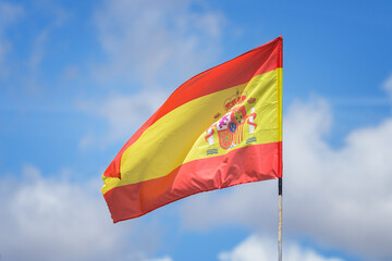 Flag of Spain waving against a blue sky with clouds