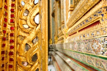 Close-up detail of decorative ceramic tiles and gilded pillars around the base of the Phra Ubosot, an ordination hall housing the Emerald Buddha inside Wat Phra Kaew (Temple of the Emerald Buddha) 