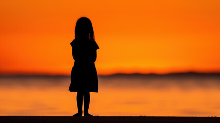 Fototapeta premium A charming silhouette of a young child against a stunning sunset beach, evoking peace and wonder.