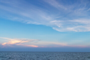 A serene ocean view at twilight, showcasing gentle waves and a colorful sky with soft clouds and a hint of moonlight.
