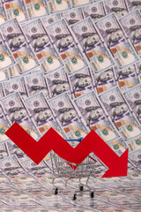 Red falling financial graph arrow and miniature supermarket shopping cart against 100 US dollar bills background