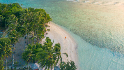 Aerial view of a man standing by the beach with a view of coconut trees and turquoise sea at...