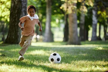 African American boy running on grass in park, he playing football alone