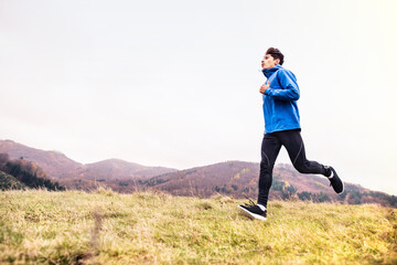 Male runner jogging in nature on dirt running trail. Morning running training for young man.
