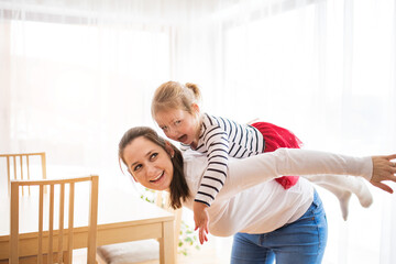Beatiful young mother carry little daughter on back, piggyback. Girl and mom having fun.