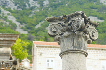 Obraz premium A close-up photo of the capital of a stone column with the Ionic order. Architectural heritage of Montenegro: a column with beautiful decoration, installed on the St. Nicholas Square in Perast.